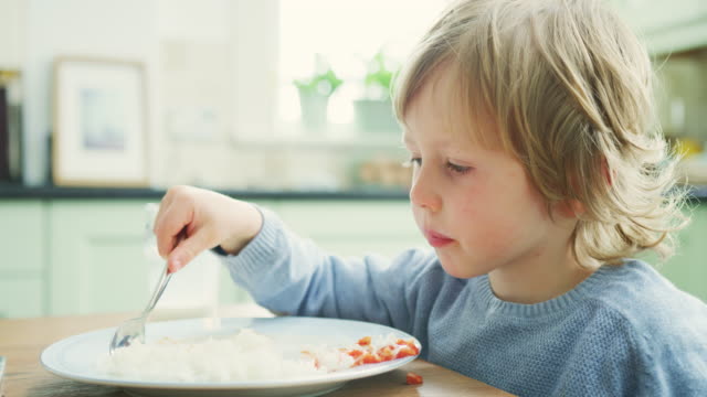 Niño-comiendo-arroz-y-salsa-con-una-cuchara-en-la-mesa