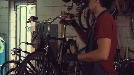 Thema-Kleinunternehmen-Fahrradreparatur.-Ein-junger-kaukasischen-Brünette-Mann-mit-Sicherheit-Schutzbrillen,-Handschuhe-und-eine-Schürze-nutzt-ein-Handwerkzeug-zu-reparieren-und-stellen-das-Fahrrad-in-der-Garage-Werkstatt