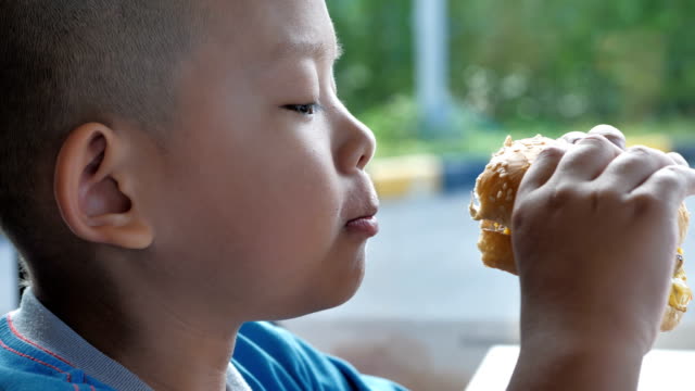 Cerca-niño-asiáticos-comer-hamburguesa,-lindo-muchacho-feliz-con-hamburguesa-en-el-restaurante.-Video-Slow-motion