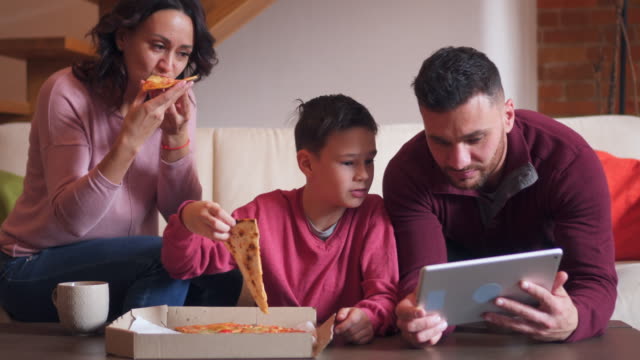 Familie-mit-Hilfe-von-digital-Tablette-während-des-Essens-Pizza-im-Wohnzimmer