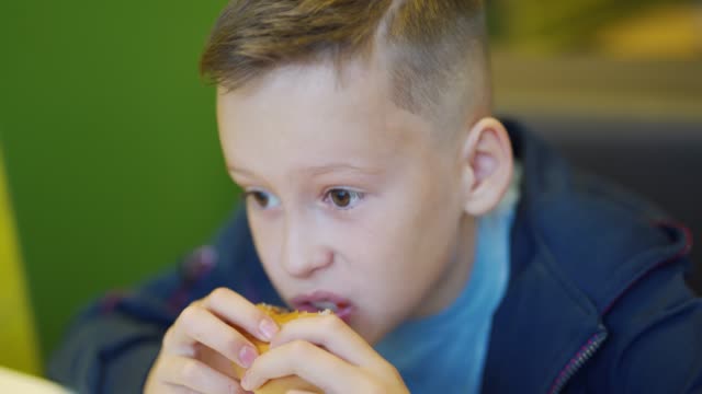 Young-teenager-eating-tasty-hamburger-in-fast-food-restaurant.