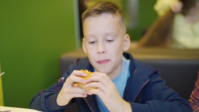 Young-teenager-eating-tasty-hamburger-in-fast-food-restaurant.