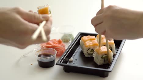Hand-takes-roll-with-chopsticks-and-sushi-in-container-delivery.