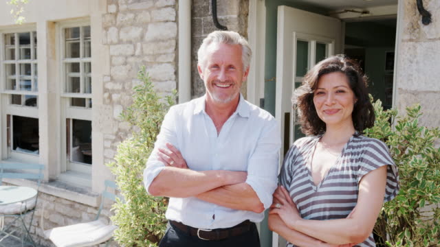 Happy-mature-couple-standing-outside-their-restaurant-pub-business-with-arms-crossed