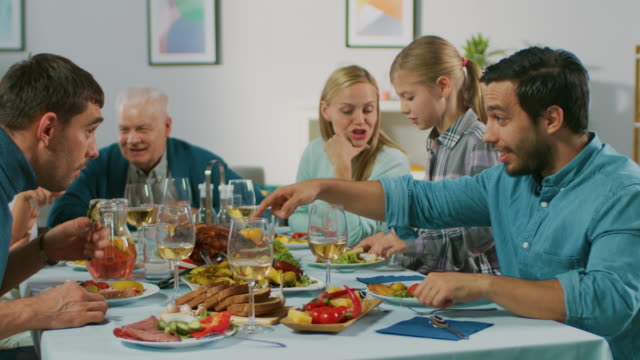 Große-Familie-und-Freunde-feiern-zu-Hause-versammelt-vielfältige-Gruppe-von-Kindern,-jungen-Erwachsenen-und-alten-Menschen-am-Tisch.-Essen,-Essen,-trinken-und-Spaß-Gespräch.-In-Zeitlupe.