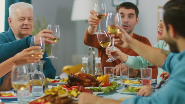 Große-Familie-und-Freunde-feiern-zu-Hause,-heterogene-Gruppe-von-Kindern,-jungen-Erwachsenen-und-alten-Menschen-versammelten-sich-am-Tisch-unterhalten-Spaß.-Gläser-klirren-und-Toast-zu-machen.-In-Zeitlupe.