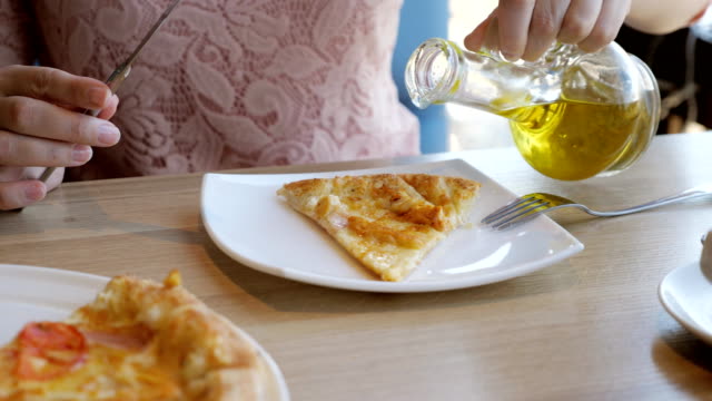 mujer-joven-en-una-cafetería-es-comer-pizza,-verter-el-aceite-de-oliva