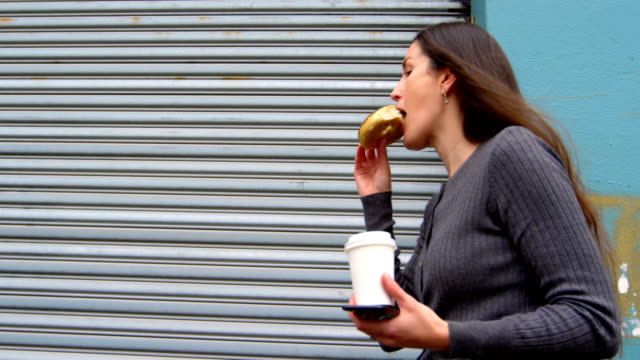 Woman-eating-donuts-while-walking-on-street-4k