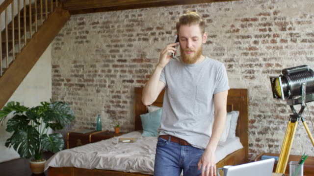 Male-Freelancer-Talking-on-Phone-in-Loft-Apartment