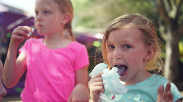 Drei-kleine-Mädchen-Essen-Zuckerwatte-und-machen-lustige-Gesichter,-die-in-Zeitlupe