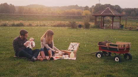 A-young-couple-on-a-picnic-with-their-baby-on-a-fall-day,-wide-angle-with-lens-flare