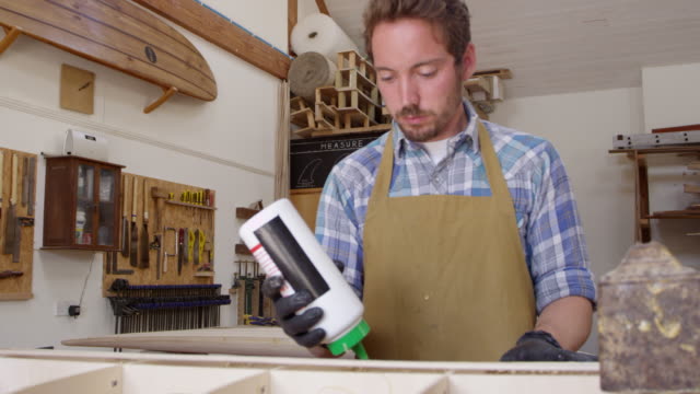 Hombre-glueing-tabla-de-surf-personalizada-en-el-taller-filmado-en-la-cámara-roja