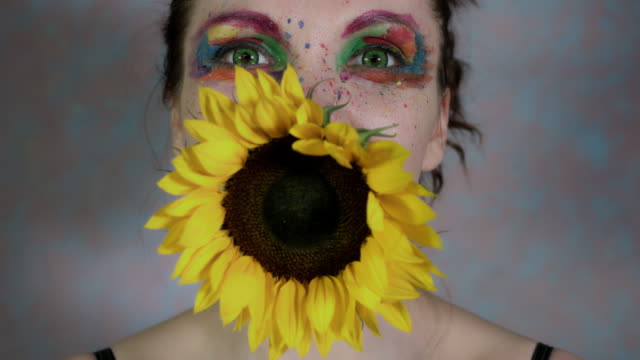 4k-Shot-of-a-Woman-with-Multicoloured-Make-up-With-Sunflower-(focus-on-face)