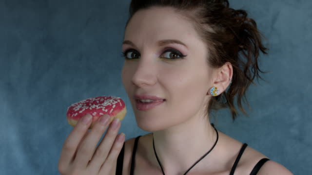 4-k-Aufnahme-einer-Frau-posiert-im-Studio-und-Essen-einen-Donut