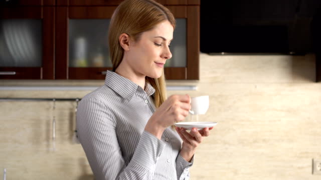 Beautiful-businesswoman-standing-in-her-kitchen-smiling.-Happy-and-relaxed-at-home.-Drinking-coffee