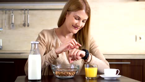 Beautiful-attractive-woman-having-breakfast,-using-her-smart-watch.-Browsing-Internet.-Reading-news