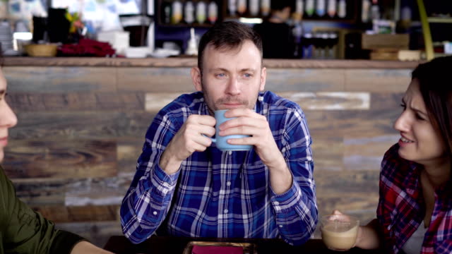 Interessant-aussehen,-ein-erwachsener-Mann-genießt-Kaffee,-der-in-einer-blauen-Tasse-gegossen-ist,-nicht-aufgepasst,-die-zwei-Mädchen,-die-in-den-Chat-im-Vordergrund
