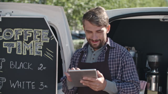 Barista-of-Mobile-Coffee-Van-Looking-at-Tablet-Outside