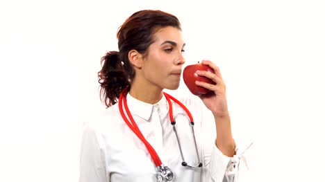 Joven-amable-mujer-nutricionista-mostrando-una-manzana-roja,-lo-muerde-y-sonriendo,-asesoramiento-dieta-saludable.-Retrato-de-joven-profesional-con-estetoscopio-y-laboratorio-capa-aislada-sobre-fondo-blanco