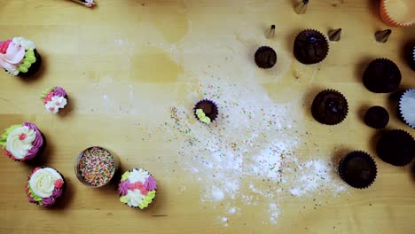 Draufsicht-der-Schokoladen-Cupcakes-auf-dem-Tisch.-Junge-Frau,-die-Muffins-mit-farbigen-Creme-aus-dem-Spritzbeutel-verzieren