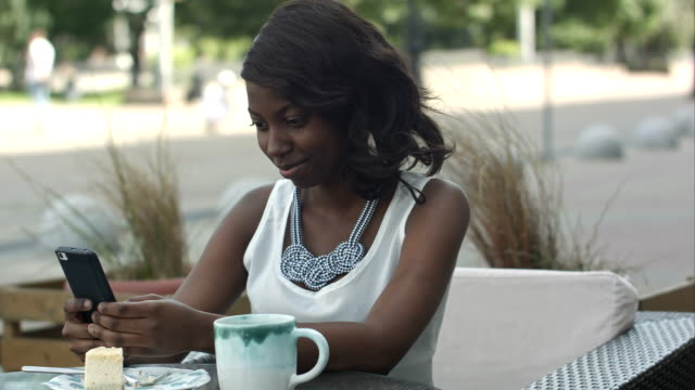 Afrikanische-amerikanische-Frau,-die-mit-Telefon,-sitzend-im-außen-café