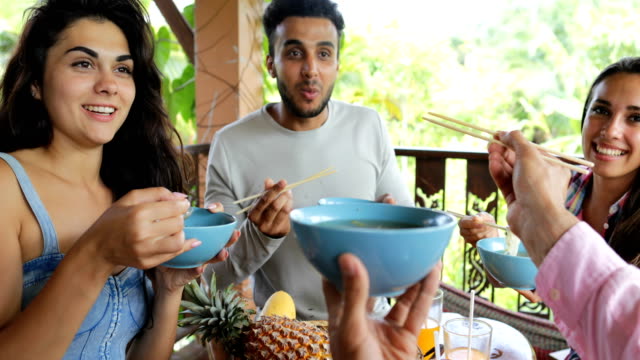 Menschen-ernähren-einander-mit-Delicious-Nudeln-asiatisch-Essen,-Freunde-Gruppe-sitzen-am-Tisch-auf-der-Terrasse-mit-Blick-auf-Wälder