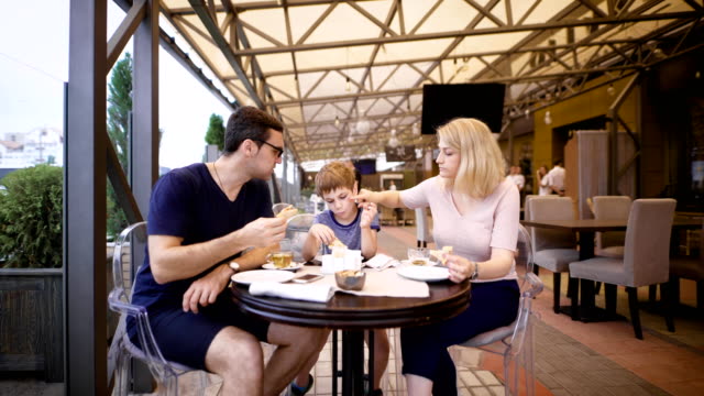 Image-of-a-happy-family-and-their-son-at-the-cafe.-Loving-couple-with-child-are-spending-time-together-in-pizzeria.-Mother,-father-and-son-relaxing-in-restaurant-eating-pizza-and-drinking-hot-tea