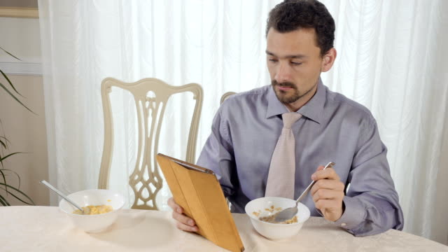 Young-businessman-eats-muesli-using-tablet