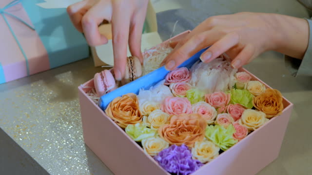 Professional-florist-making-gift-box-with-flowers,-cake-macarons-at-flower-shop