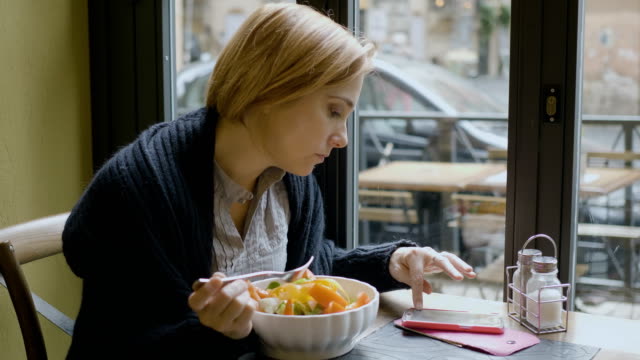 eine-Frau-Essen-einen-Salat-und-Überprüfung-auf-neue-Nachrichten-auf-ihrem-smartphone