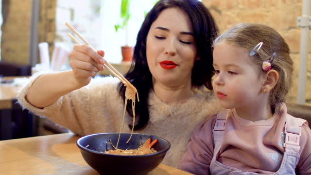 Junge-Mutter-ihre-kleine-Tochter-zu-ernähren,-mit-einer-koreanischen-Nudeln-im-restaurant