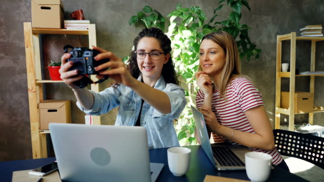 Diseñadores-creativos-están-posando-para-selfie-juntos-sentados-en-la-oficina-moderna.-Son-con-cámara,-riendo-y-socializar.-Concepto-de-estilo-de-vida-juvenil.