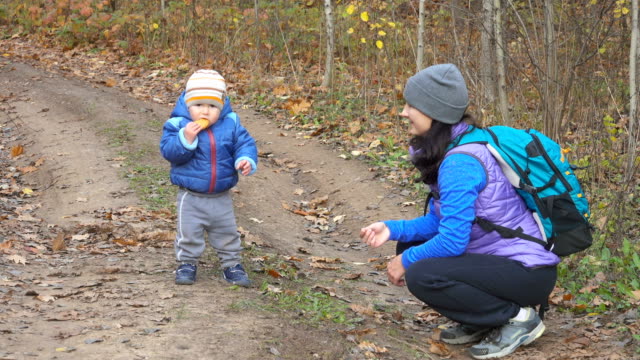 A-mother-feeds-her-little-child-in-autumn-forest-on-the-trail.