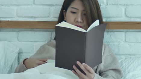 Hermosa-mujer-asiática-disfruta-de-beber-café-caliente-y-lectura-en-cama-en-su-dormitorio.-Mujer-de-Asia-usando-suéter-cómodo-sosteniendo-un-libro-y-una-taza-de-coffee.lifestyle-mujer-de-asia-en-el-concepto-de-hogar