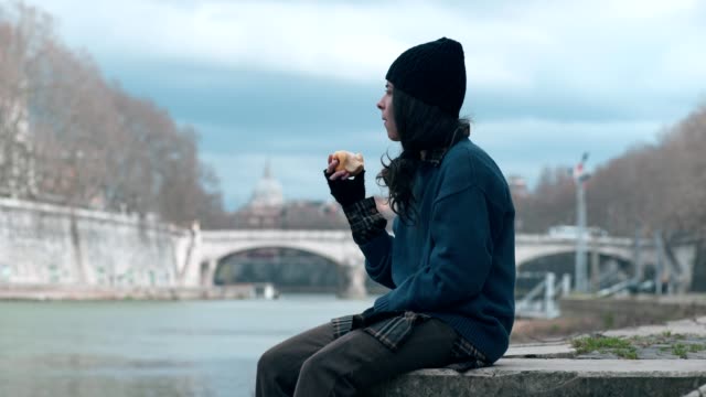 einsame-junge-Obdachlose-isst-einen-Apfel,-den-Fluss-zu-betrachten