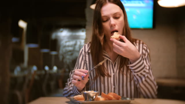 Young-beautiful-woman-brunette-smears-pate-on-a-piece-of-bread-in-cafe-with-knife.-And-she-eats-sandwich.