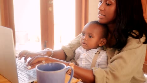 Blogger-mother-with-baby-boy-working-from-home-on-laptop