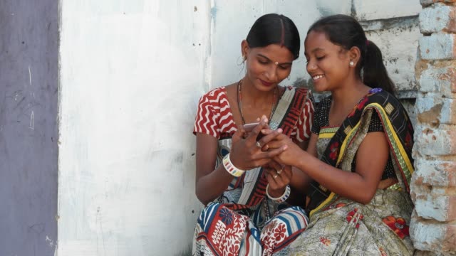 Two-Indian-women-dress-colorful-buddies-laugh-and-share-photo-video-secrets-love-on-the-phone-fight-tussle-and-show-and-tell-communicate-talk-discuss-static-shot-two-medium-shot-staircase-brick-home
