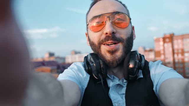 Happy-creative-musician-man-or-dj-in-headphones-on-neck-taking-selfie-using-camera-or-smartphone