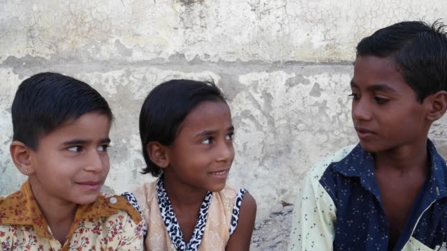 Drei-indische-Kinder-sitzen-und-miteinander-zu-reden-und-sich-dann-in-Richtung-der-Kamera
