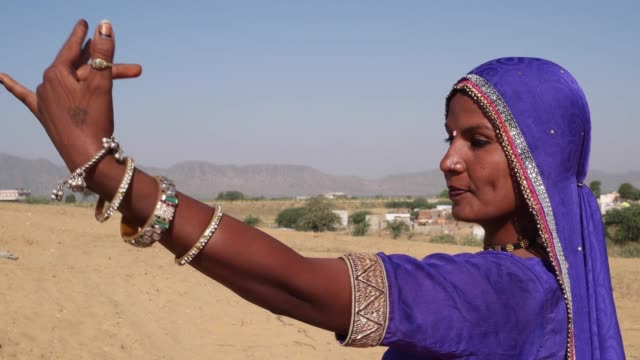 Nomadische-Frau-tanzt-auf-einer-Sanddüne-in-Rajasthan-mit-Kamelen-im-Hintergrund