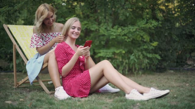 two-friends-have-a-good-time-in-the-park,-they-use-a-smartphone