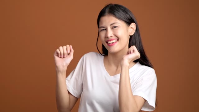 Joven-bailando-aislada.-Mujer-asiática-en-camiseta-blanca-bailando-gracioso-sobre-fondo-naranja.