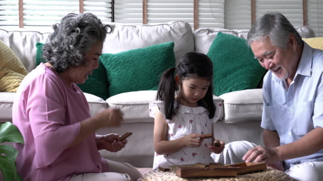 Couple-senior-and-kids-girl-playing-puzzle-games-together-in-living-room-at-home.-Concept-of-caucasian-family,-education,-growing-learn-and-development-of-age.-4k-resolution.
