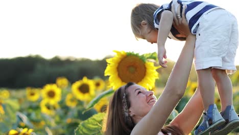Eine-junge-Mutter-und-ein-kleiner-Junge-stehen-auf-einem-Feld-mit-Sonnenblumen.