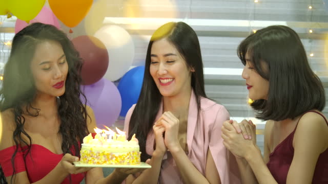 Young-woman-birthday-girl-is-making-wish,-blowing-candle-on-cake-and-clapping-hands-while-her-friends-are-congratulating-her-at-the-party.--Slow-Motion