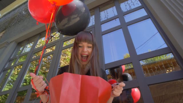 Shopping-junge-Frau-erstaunt-schauen-in-Papiertüte-und-glücklich-lächelt-vor-schwarzem-Hintergrund-mit-Luftballons