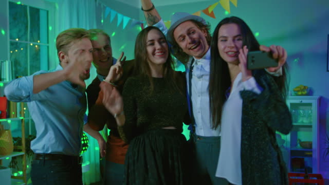Glückliche-Gruppe-von-jungen-Leuten-unter-kollektiven-Selfie-auf-wilde-Hausparty.-Neon-Licht,-Disco-Kugel-und-lustige-Kostüme.