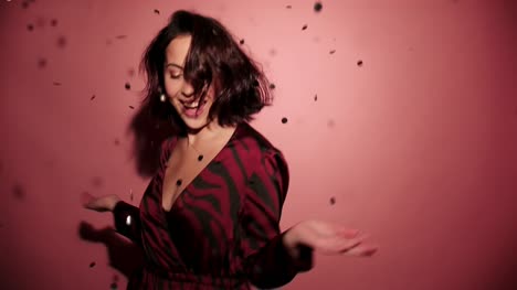 Brunette-happy-woman-run-into-the-shot-and-start-to-spin-and-then-run-out-with-confetti-in-pink-background-wear-red-dress