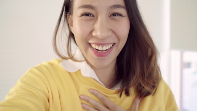 Asian-blogger-woman-using-smartphone-recording-vlog-video-in-living-room-at-home,female-enjoy-funny-moment-while-lying-on-the-sofa-when-relax-at-home.-Lifestyle-blogger-making-video-at-home.